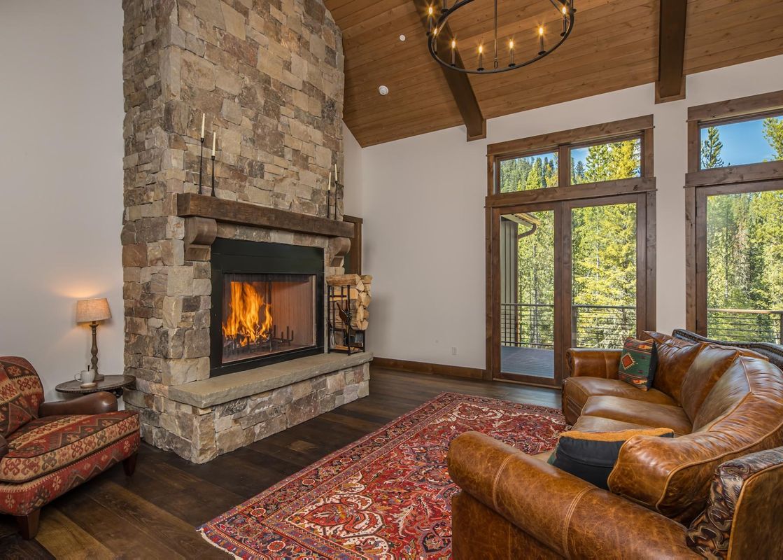 The living area of Stony Creek Chalet features a cozy stone fireplace, plush leather seating, and large windows that offer a beautiful view of the surrounding forest.