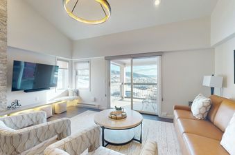 A modern living room in Torian Plum Plaza 804 with a leather sofa, two armchairs, a large TV, and a balcony overlooking a snowy mountain landscape.
