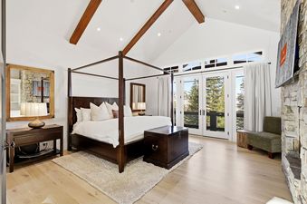 Primary bedroom with a four-poster bed, vaulted ceilings, and glass french doors showing a forest view.