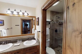 The bathroom in Manor Vail 267 features a large, well-lit vanity with dual sinks and a large mirror, with a separate shower room behind a glass door.