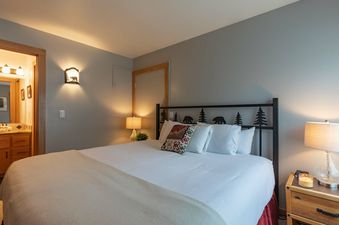 Cozy bedroom with a rustic metal headboard, warm lighting, and a view into the en suite bathroom.