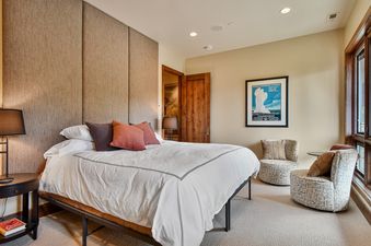 A serene bedroom in the Sky Villa features a bed with white linens, two decorative chairs, and a framed Yellowstone National Park poster on a neutral-toned wall.