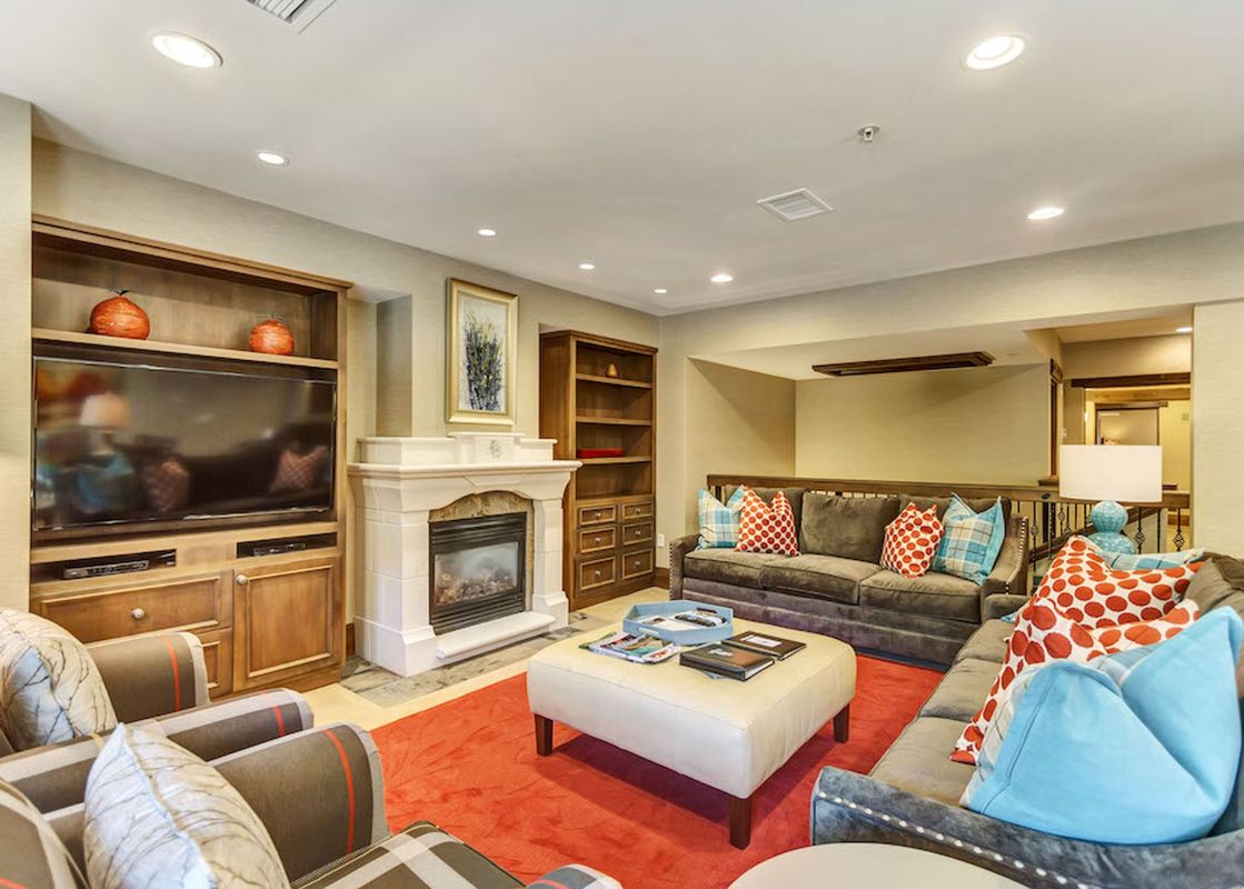 The living room at The Chateaux Four Bedroom Residence features a fireplace, a flat-screen TV, a plush red rug, and comfortable sofas.