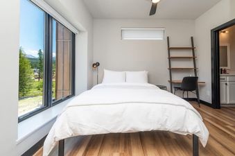 The bedroom in Luxury Alpine Abode features a comfortable white bed, modern furnishings, and large windows offering a scenic mountain view.