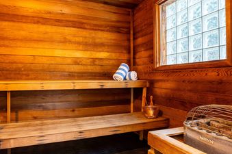 A private sauna at Montaneros 420 features wooden walls and benches, a sauna heater with a copper bucket and ladle, and a glass block window, with two striped towels resting on the bench.