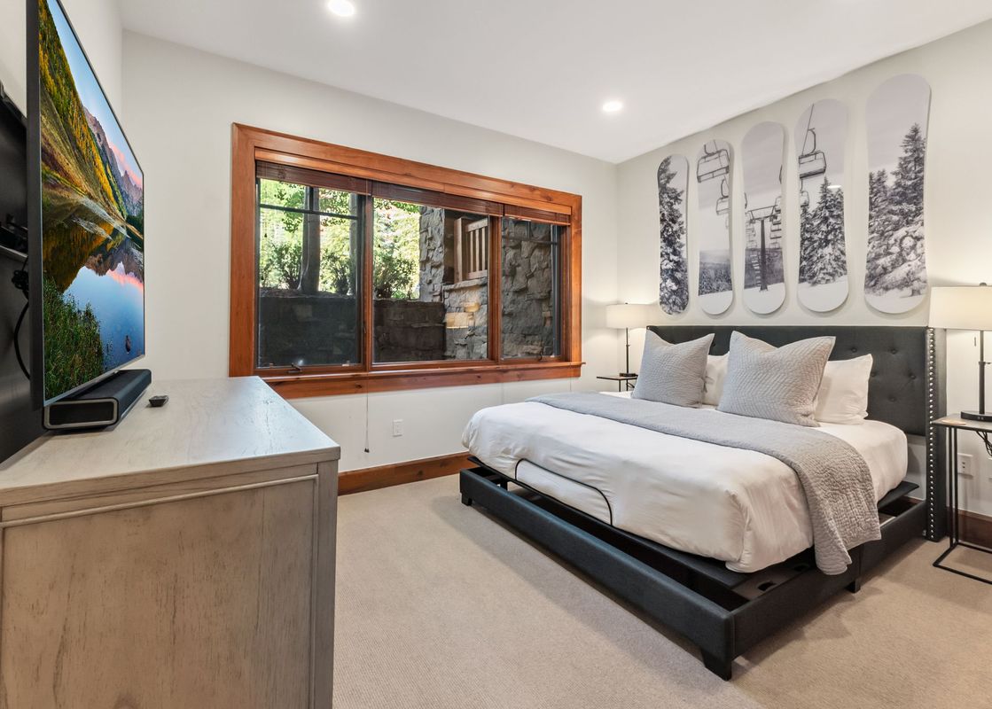 A cozy bedroom with a king bed, decorated with snowboard-themed art, a large window, and a wall-mounted TV.