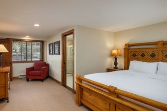 A cozy bedroom featuring a large wooden bed, a red armchair, and an adjacent bathroom at Montaneros 418.