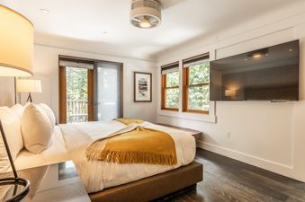 The spacious bedroom at Cedar Crest Eagle Cottage 8 featuring a large bed, a wall-mounted TV, and a balcony entrance.