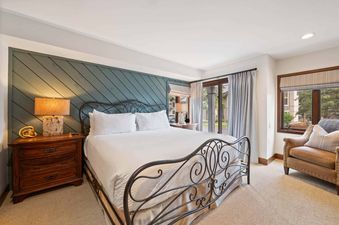 A king bedroom in Ridgepoint Townhome 192 with a wrought iron bed, teal accent wall, and cozy armchair by a window.