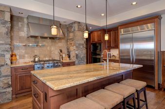 The kitchen in Moonlight Basin 20 Peaks View has a stainless steel stove and refrigerator, a large island with seating, and a view of the mountain range from the windows.