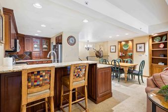 A spacious living room with a wooden dining table and chairs, a large kitchen with a breakfast bar, and a comfortable couch