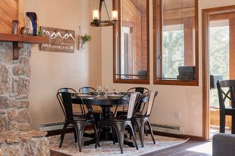 A cozy dining area featuring a round black table set for six, surrounded by dark metal chairs.