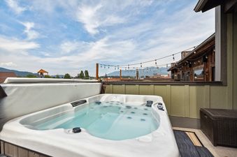 A private hot tub on a rooftop deck at Baker Loft 302, offering expansive views of mountains and the sky.