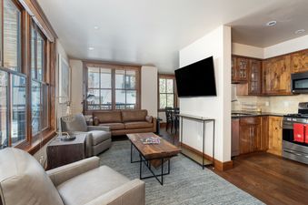 A spacious living area flows into the kitchen with warm wood accents, two comfortable sofas, and a large flat-screen TV.