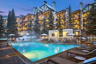 An evening view of Montaneros 220's heated outdoor pool, hot tubs, and snow-dusted alpine lodge, illuminated against a twilight sky.