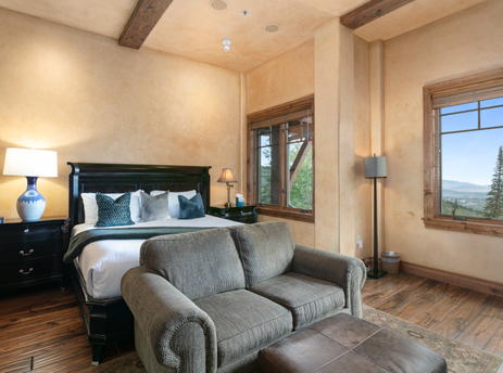 Grand Lodge Studio 205 boasts a comfortable living area featuring a plush couch, a large window showcasing a stunning mountain vista, and a plush bed with pillows.