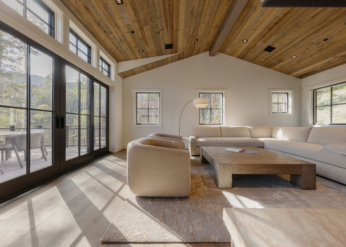 A bright living room with a large sectional sofa, wooden coffee table, and expansive windows looking out onto a mountain landscape.