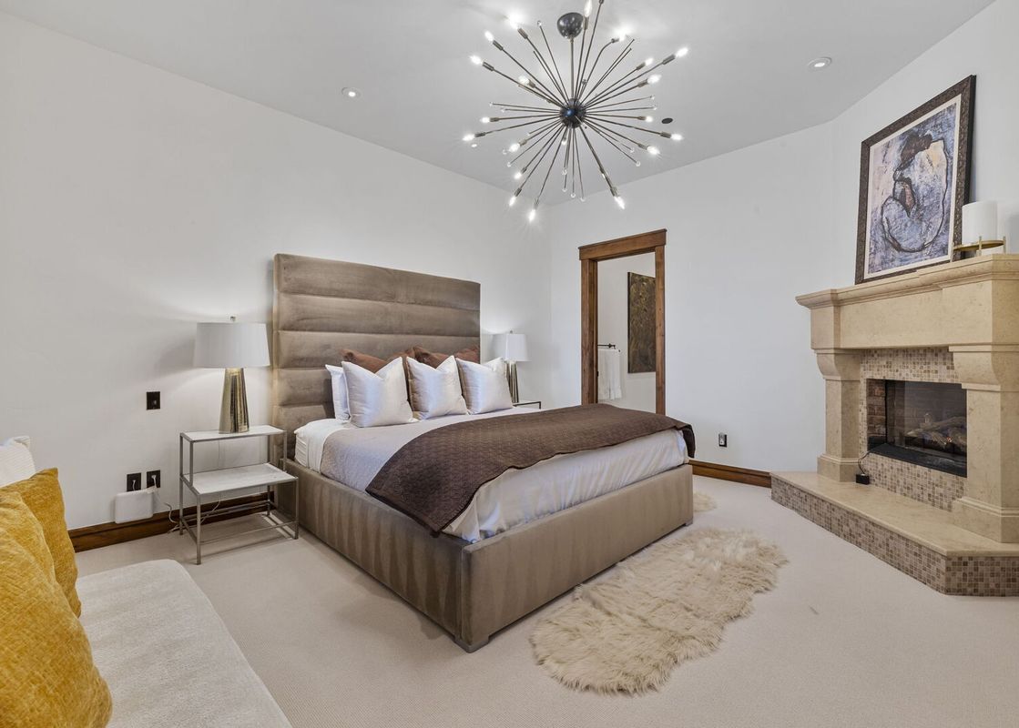 A luxurious bedroom at Silver Horse at The Colony with a king-sized bed, fireplace, and modern chandelier.