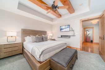 A king-size bed with a white comforter and grey pillows sits in the center of a bedroom in Lumiere Two Bedroom Penthouse.