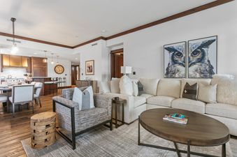 Living area of Arrowleaf 209 with an L-shaped sofa, armchair, and view of the kitchen and dining areas.