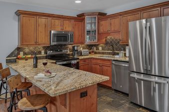 A fully equipped kitchen with wooden cabinetry, granite countertops, and stainless-steel appliances in First Tracks Chalet.