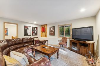 A cozy basement living area with a large brown leather sectional sofa, a wooden coffee table, framed posters, and a television on a wooden media console.