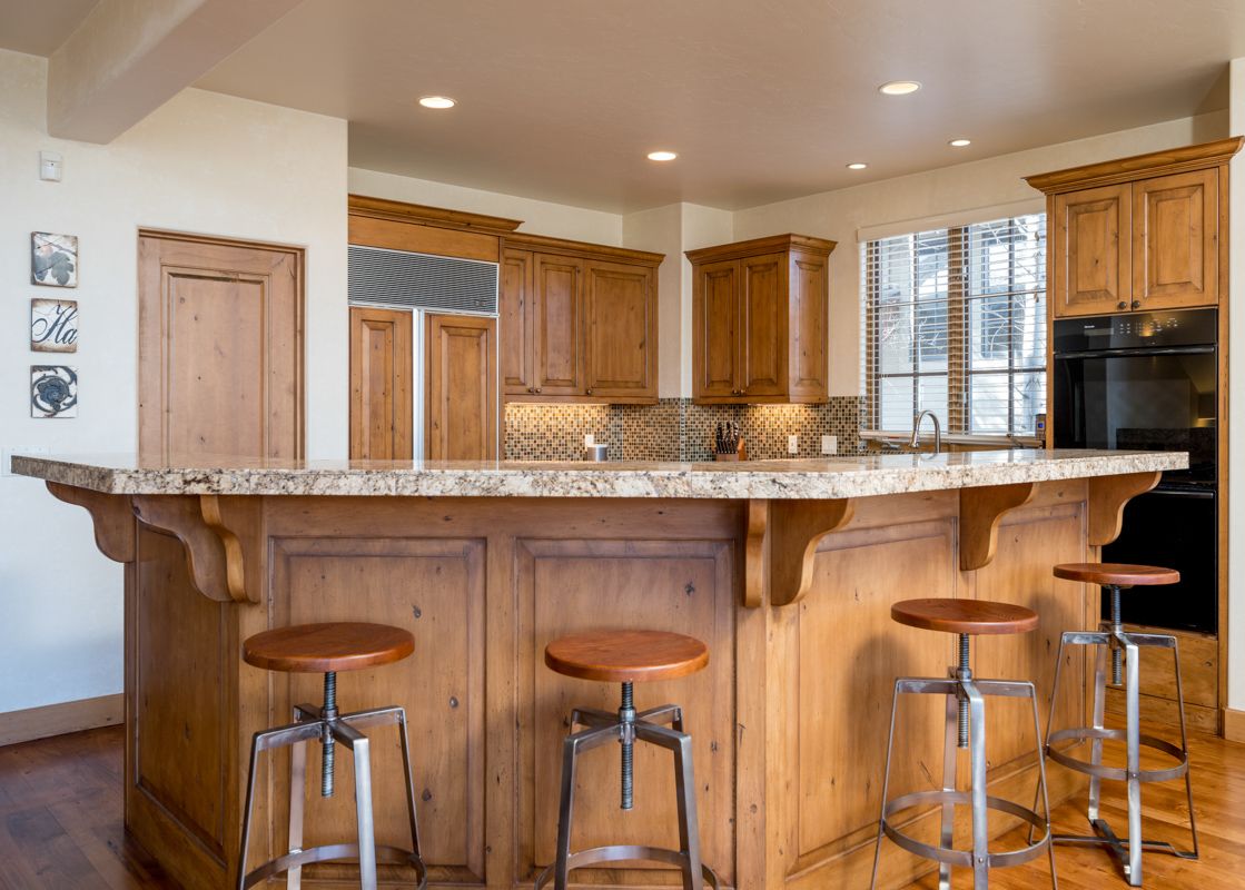 A kitchen island with bar seating and a granite countertop in a luxury home with a wood-paneled kitchen.