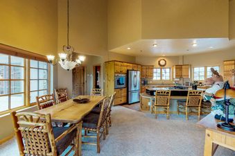 The dining area and kitchen of Westermere 410, featuring a rustic wooden dining table and chairs, with a fully equipped kitchen in the background.