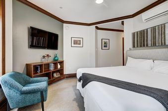 A cozy bedroom at Snow Cloud Lodge 515 with a king-sized bed, a flat-screen TV, a wooden console, and a teal armchair.