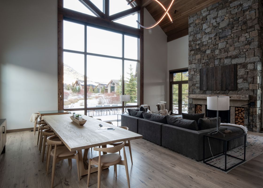 A large dining table and living area with a stone fireplace and floor-to-ceiling windows at The Lodge at Shooting Star West 01.