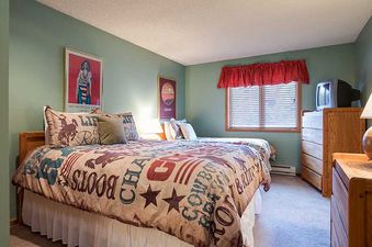 A cozy bedroom with two beds featuring rustic-themed bedding, wooden furniture, and green walls, providing a comfortable retreat at Ranch at Steamboat RA103.