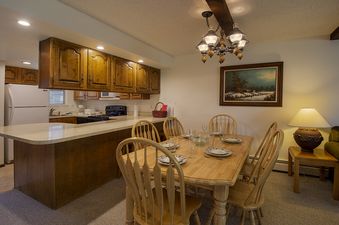 A dining table set for a meal sits in an open-concept living space with a kitchen and a bar area, featuring wood cabinetry and white appliances.