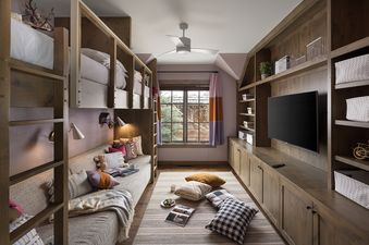 A cozy bunk room at Fish Creek Lodge 05 features custom wooden bunk beds, a daybed with colorful pillows, an entertainment center with a television, and a window with vibrant drapes.