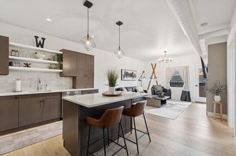 An inviting open-concept living area in the Bear Den, featuring a modern kitchen with dark wood cabinets and a stylish island with seating, flowing into a comfortable living room with contemporary decor and hardwood floors.