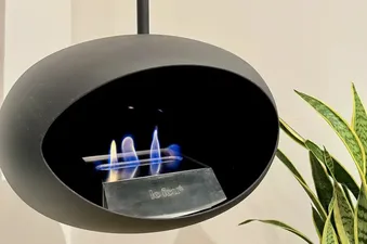 A modern black spherical bioethanol fireplace with blue and yellow flames is shown, with a green snake plant to the right.