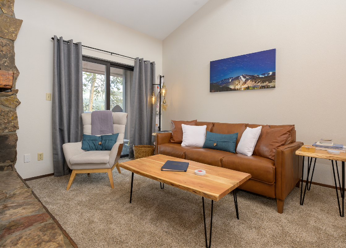 A cozy living room in Beaver Village 833 features a comfortable brown leather sofa, a light-colored armchair with teal and purple throws, and a wooden coffee table, all set on a light-colored carpet.