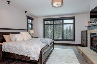 A bedroom in the Moonlight Basin 6 Jakes Lane with a king-size bed, a fireplace, and a view of the snowy forest.