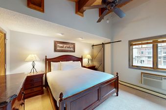 A comfortable bedroom with a large bed, nightstands, and a ceiling fan, illuminated by natural light and lamps.