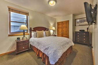A cozy bedroom with a large bed, wooden furniture, and a wall-mounted TV.