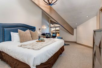 A bedroom in Abode at Little Belle 3 features a plush king bed and seating area under a sloped roof.