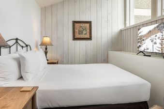 A cozy bedroom in Vantage Point 504 featuring a king-sized bed with white linens and a television displaying a snowy mountain scene.