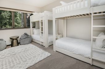 The Chateau Tremonte 8 bunk room featuring two white bunk beds, gray bean bags, a bronze side table, and a window with a green exterior view.