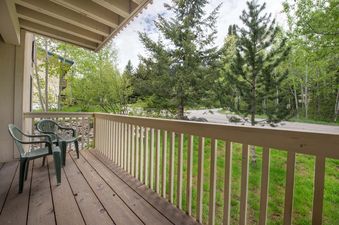 A private covered balcony at Whiteridge B5 featuring seating and scenic views of surrounding green trees and a grassy lawn.