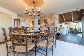 The dining area in Peaks Penthouse 846 features a large wooden table set with placemats and glasses, surrounded by wooden chairs with woven seats, all beneath a decorative chandelier.