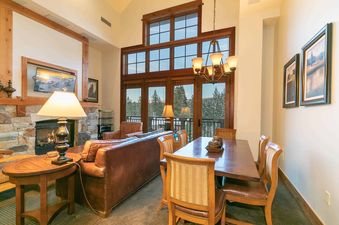 A spacious living room with a fireplace, large windows with views of a snowy mountainside, and a dining table with chairs
