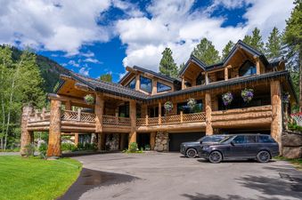 The exterior of the luxurious Northstar Chalet, a grand log cabin with multiple gables, large windows, and a wide balcony adorned with floral hanging baskets.