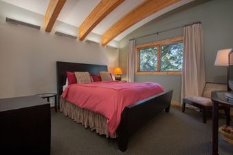 A cozy bedroom in Westbrook House with a red bed, wooden ceiling beams, and a window with forest views.