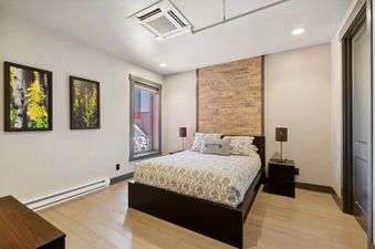 A cozy king bedroom in Lupfer Unit D with a wood accent wall, elegant bedding, modern nightstands, and nature-themed artwork.
