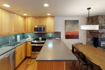 The kitchen in Manor Vail 121 features stainless steel appliances, a large counter, and a dining area with a wooden table and chairs.