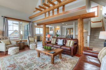 The spacious main living area of Saddle Ridge Townhome Unit B1 features a large leather sectional, a rustic coffee table, and an intricate area rug, with views of a snowy exterior through large windows.